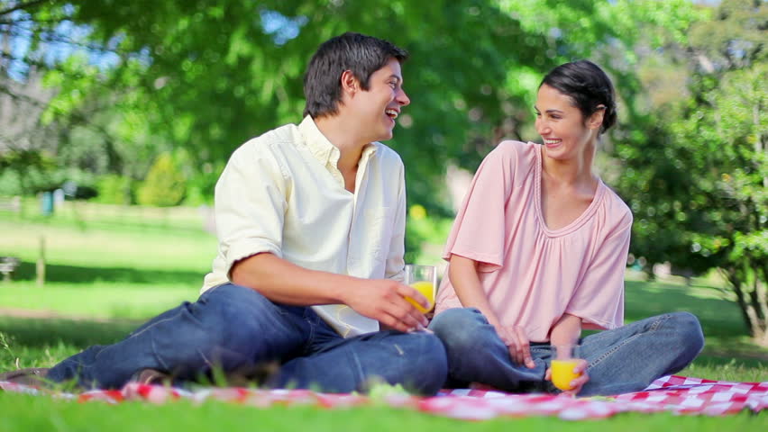 Laughing couple drinking orange juice in a parkland