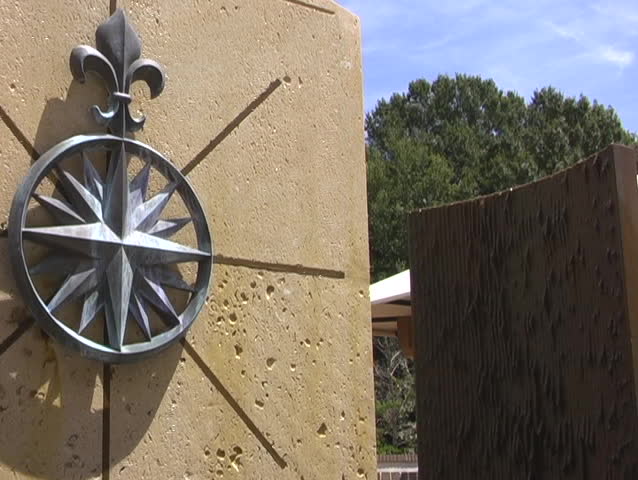 A large outdoor fountain sculpture with a metal emblem on one part has clear water running down it.