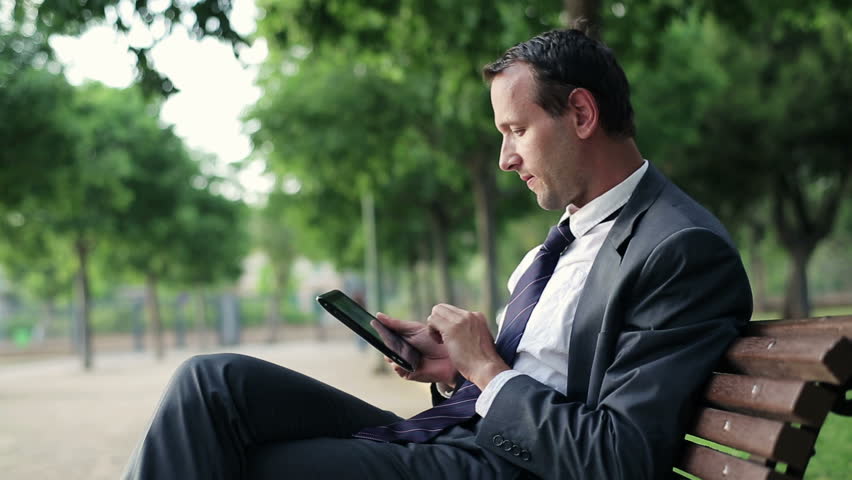 Young businessman working on tablet computer in the park, dolly shot
