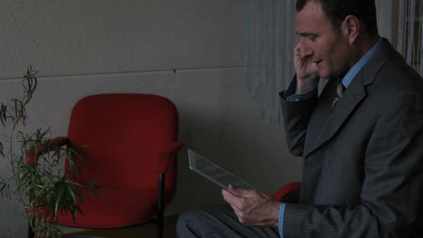 man is calling in an office with a mobile phone and watching images op his tablet computer
