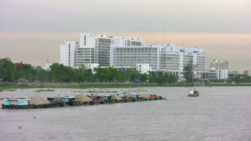 Passing a tug towing a string of barges down the Chao Phraya River in the north of Bangkok, Thailand. Building in background is the Ministry of Commerce. Canon HV20, HD 1080-50i.