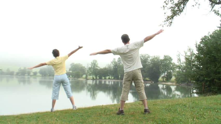 HD 1080i: Couple doing gymnastics early in the morning at a lake in the mist