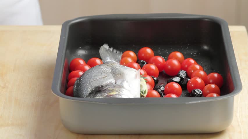 Laying seabream on tomatoes and olives and brushing it with herb oil