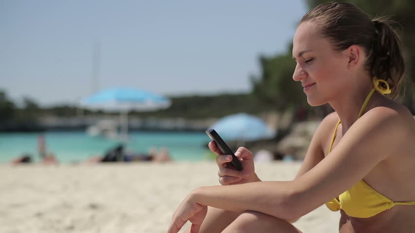 Young woman using cellphone on the beach, dolly shot