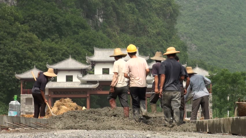 YANGSHUO - AUGUST 10 2010: Workers are pulling a plough in a rural area in China, with a traditional (newly erected) pagoda style building in the background, in Yangshuo