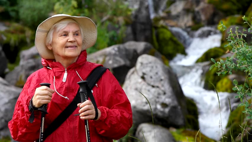 senior woman waves near a waterfall 