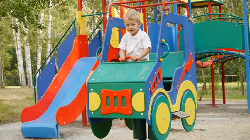 Happy boy swinging in toy car on children playground.