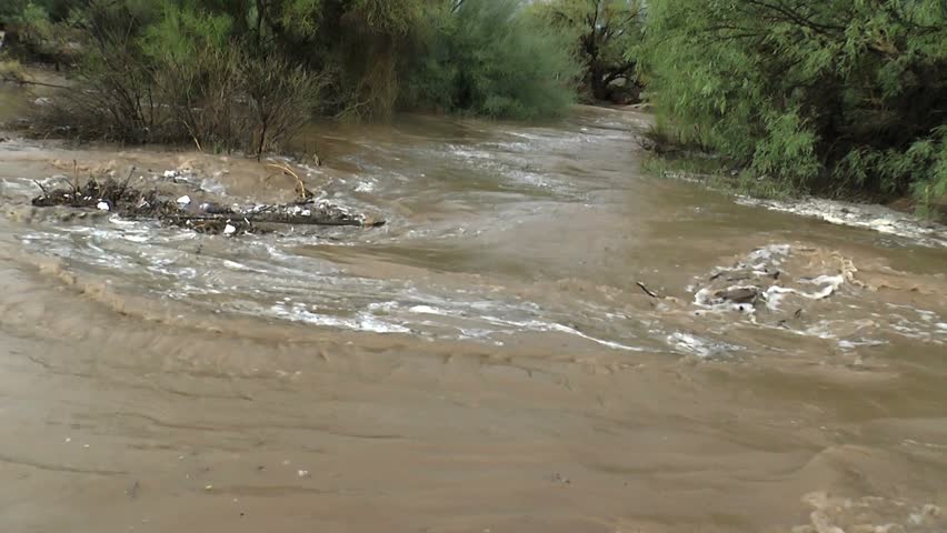 Plastic bottles, wood, assorted debris, swept into piles after heavy rains, swirl in eddies through flooded backyards. 1080p