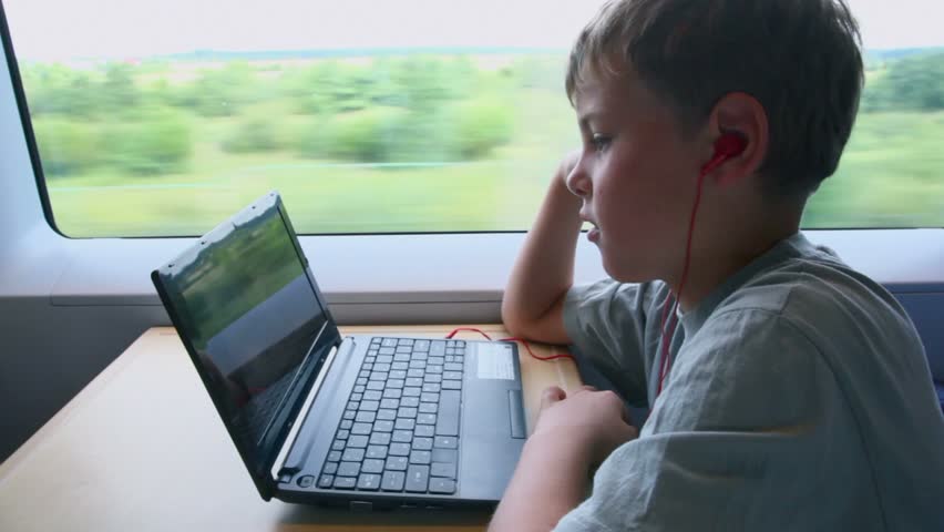 Little boy watch on netbook when sits at train near window