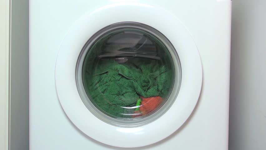 circular door of white washing machine running and turning with colored clothes
