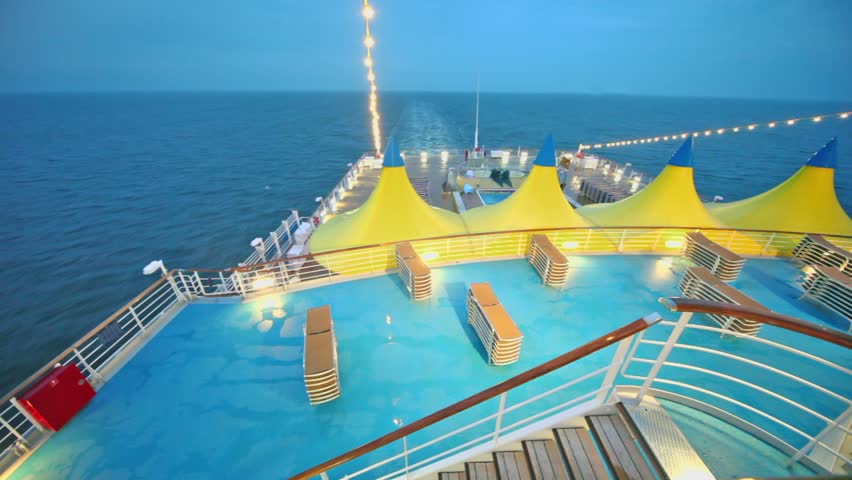 Sunbeds near pool and tents on empty deck of ship which float in sea at evening during cruise