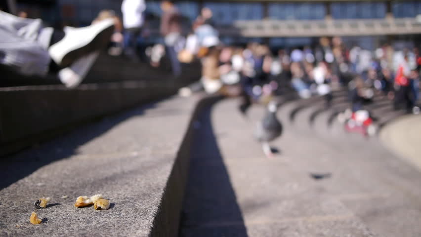 A pigeon eats some scraps of food on some steps in a busy city square.