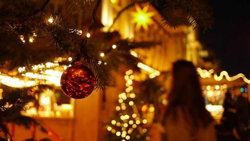 Shoppers at an open-air market at christmas. Foreground is a christmas tree. Shoppers are blurred. Nightime.