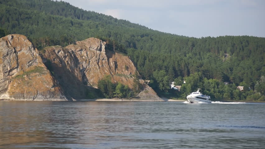 White pleasure boat and a fishing boat are floating on the Siberian Yenisei River on the background of mountainous coast line. Static shot.
