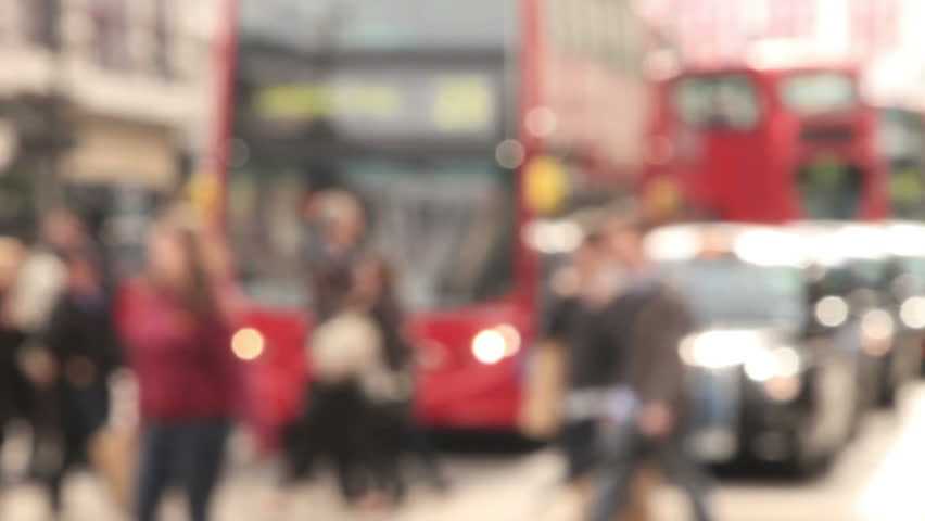 Unrecognizable and blurred pedestrians cross Oxford Street in front of buses and taxis in London