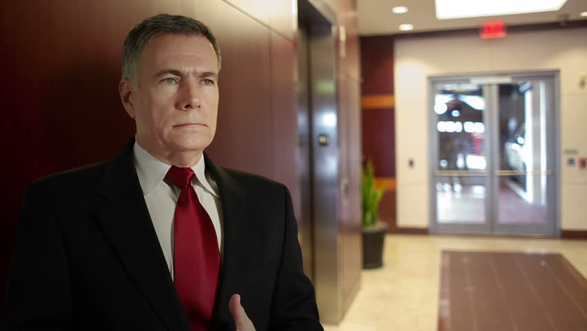 An attractive mature businessman waiting in a office building lobby area checks his watch.