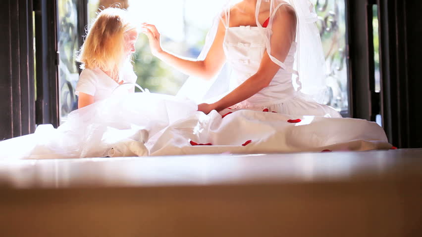Little bridesmaid sitting with young bride wedding dress playing flower petals
