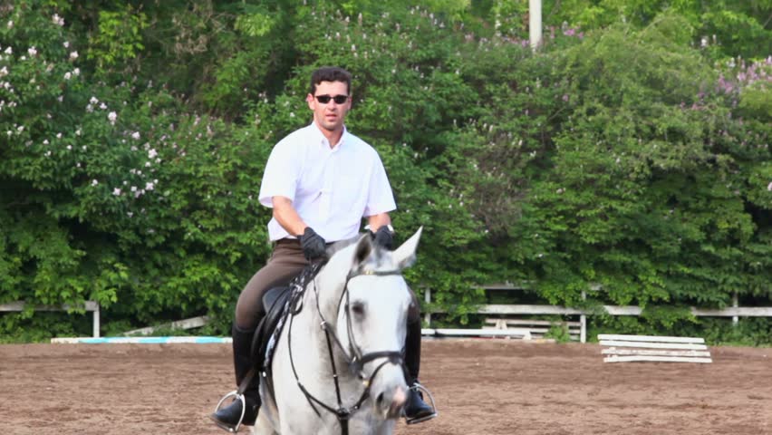 Horseman in sunglasses approach on horseback by equestrian field at summer day