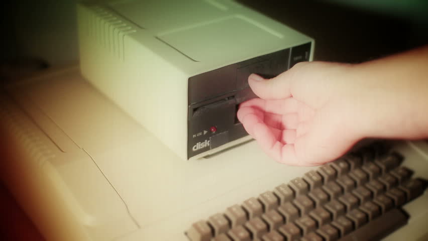 Old film look treatment of a close-up of inserting and removing an old-style 5.25" floppy disk.