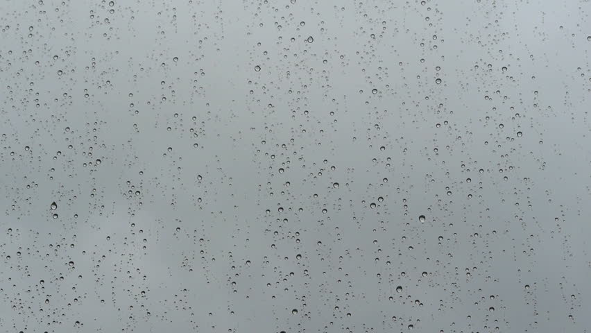 Beads of rain on a window. Gray sky background. Camera move then hold.