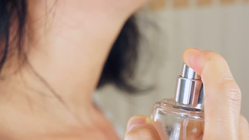 Short focus, close up shot of a woman spritzing perfume out of a bottle onto her neck.