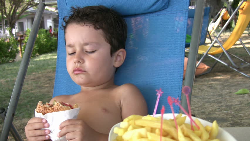 Little boy eating burger and fries in lounge chair