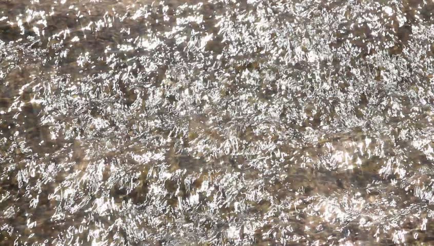 Water shined with the sun flows down on stones