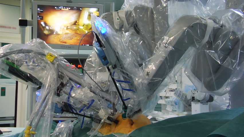 Robot performs heart surgery. Monitor shows procedure in background. 