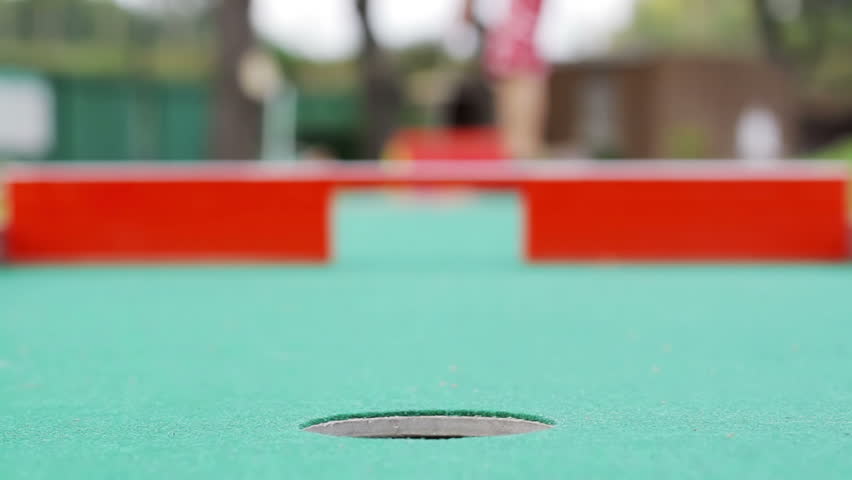 Young woman playing mini-golf during cloudy day, selective focus, successful attempt