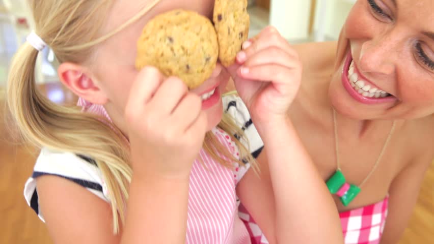 Daughter holds up two cookies over eyes and makes face before covering the camera with them.