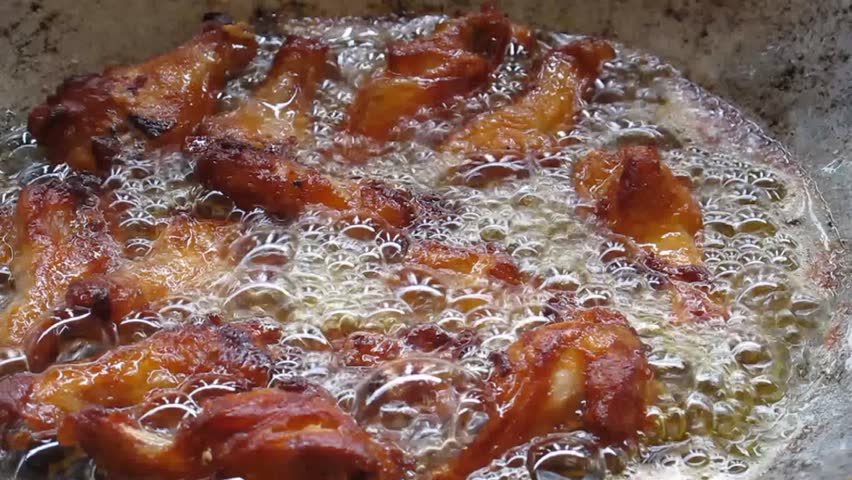Chicken drummets deep frying in oil in a cast iron frying pan
