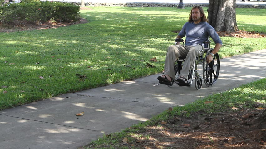 Paraplegic veteran pushes himself in his wheelchair down a sidewalk in a city park.