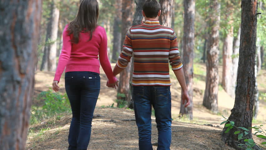 Lovely couple holding hands strolling away in the woods