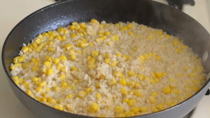 Rice and corn being stirred while cooking in pan on stove