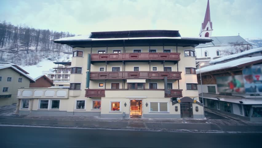 Car passes by street in small town near mountain with forest on winter day