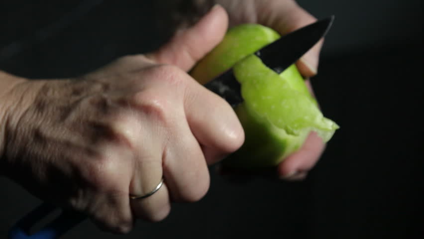 Woman peeling green apple with knife on dark background close up HD 1080p
