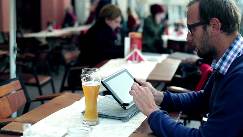 Young man with tablet computer drinking beer in the restaurant, outdoors
