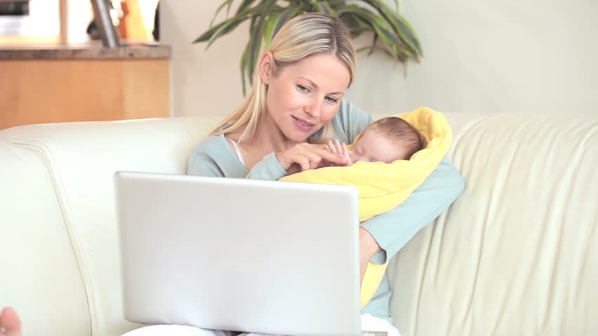 Woman holding a child in a blanket while she is making a video call on a laptop