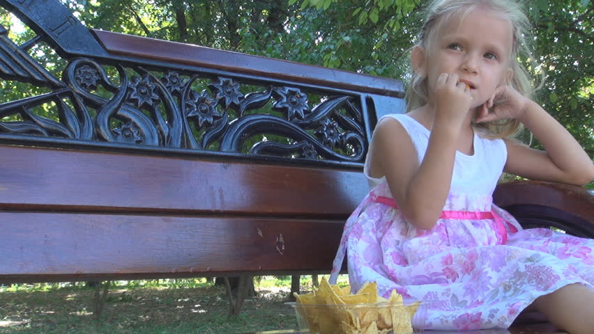Little Girl Eating Cornflakes on a Bench in Park, Child Feeding Herself