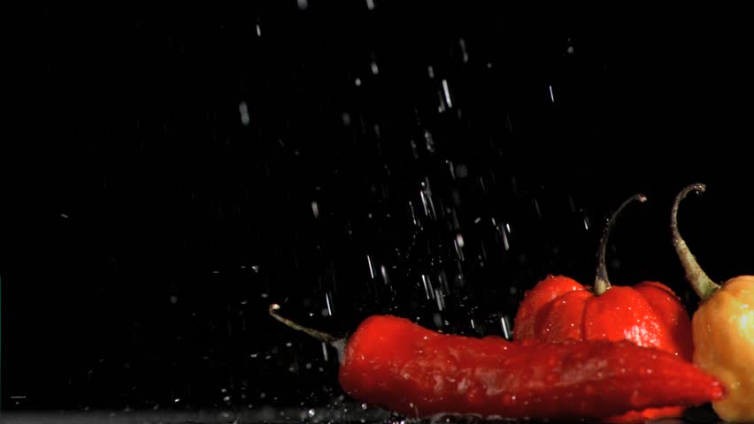 Spicy vegetables in super slow motion receiving drops of water against a black background