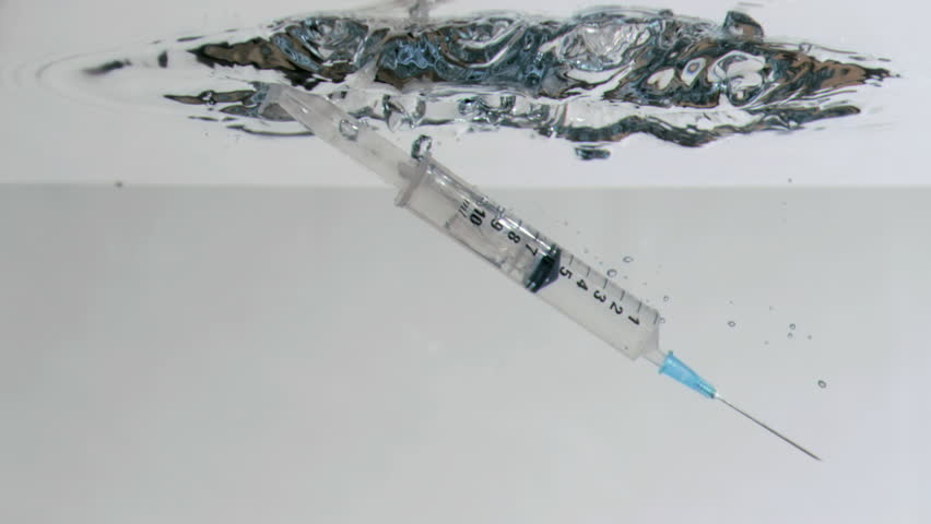 Syringe in a super slow motion falling in the water against a grey background