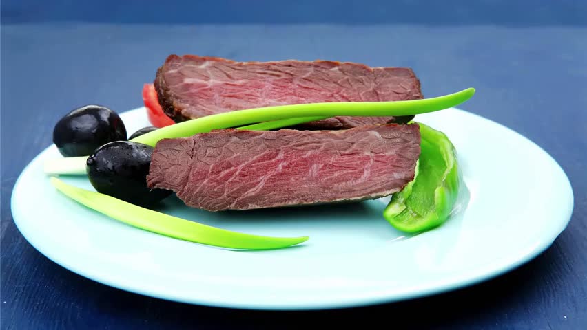 meat savory : grilled beef fillet mignon on blue plate with pepper chives and black greek olives over blue wooden table