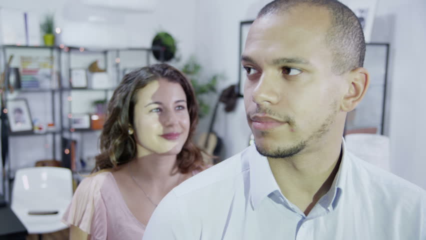 Young woman wraps her arms around her partner from behind and they both look away from camera