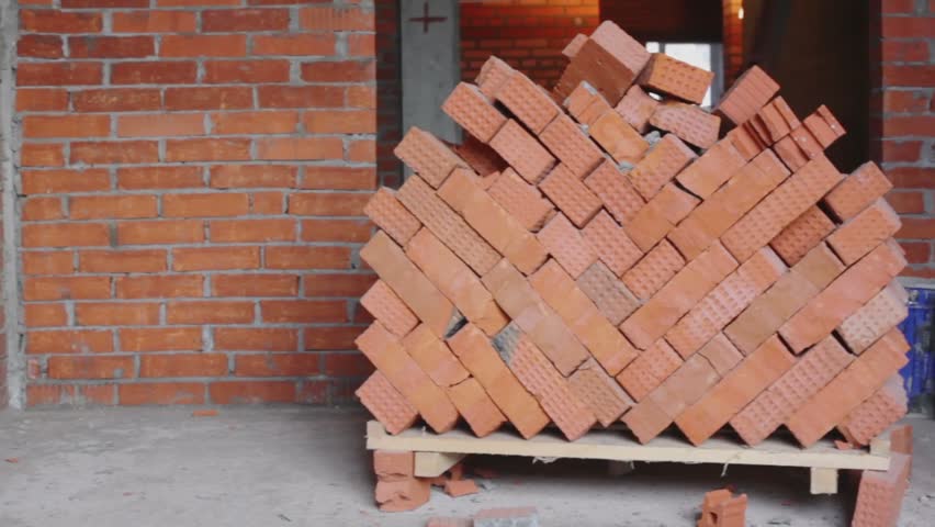 Red brick stack near wall in room at construction site, closeup view in panoramic motion