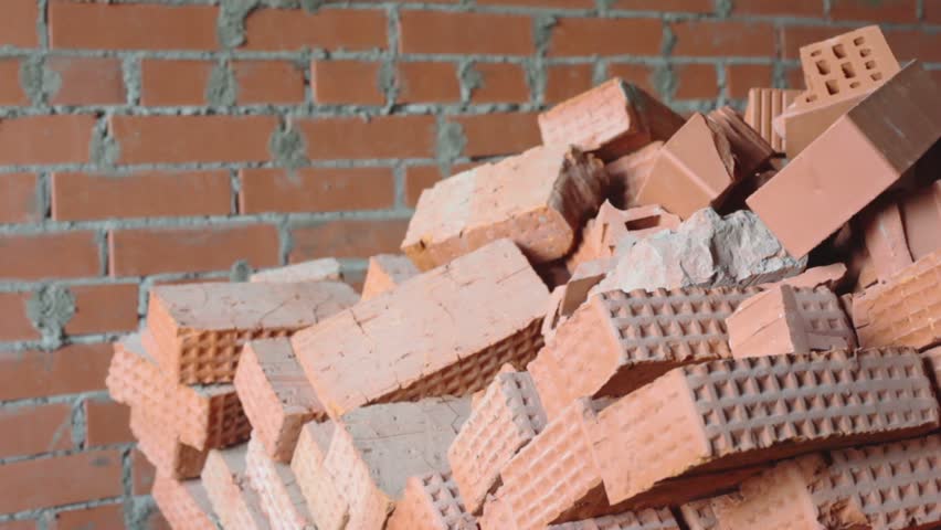 Red brick stack near wall, closeup view in motion at construction site