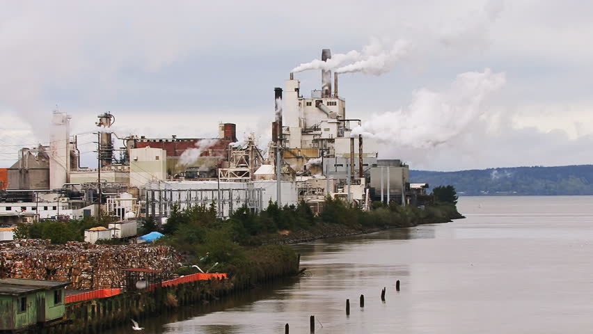 A large industrial mill belching steam/smoke from multiple stacks.