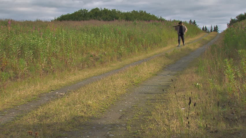 Guy in a hat walking with a gun wile looking around.