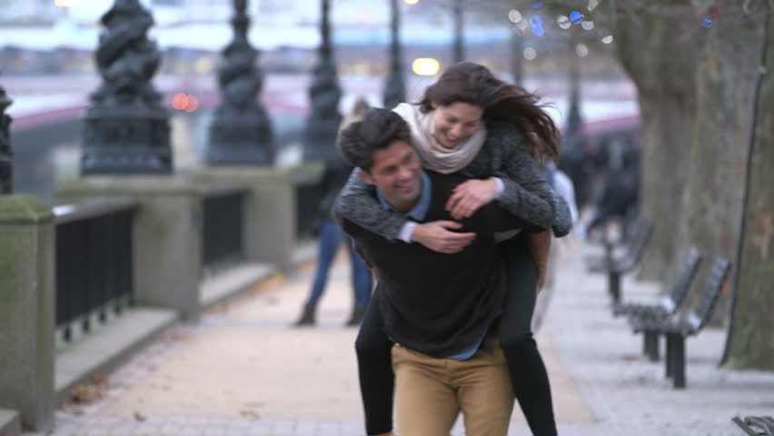 Piggyback. Casually dressed heterosexual couple having fun together in a big city. They are running and laughing.