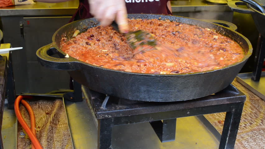 Hand with tool mix slumgullion meal cooked in big pot in outdoor street fair.