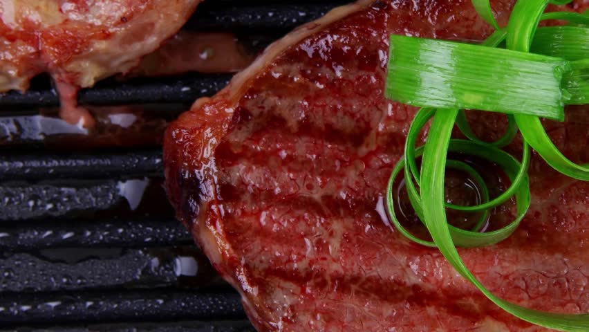 roast bloody beef fillet steaks on black teflon grill plate with green leaves isolated on white background